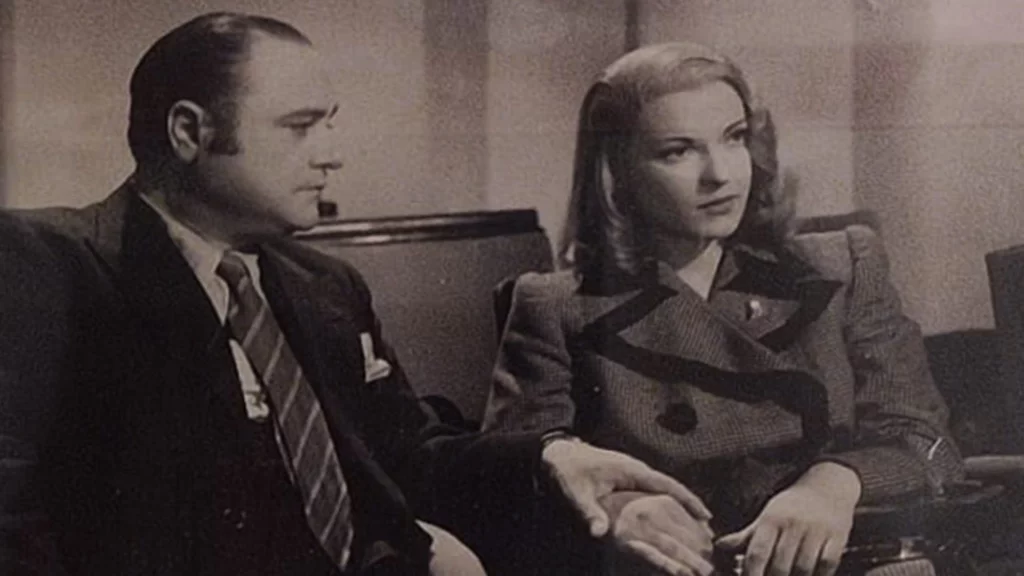 Fotografia di Beniamino-Gigli seduto su una poltrocina che guarda l'attrice seduta al suo fianco e le tiene la mano